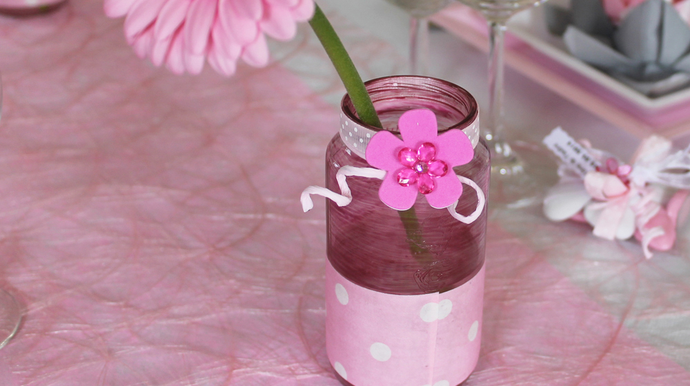Ce vase décore votre table avec légèreté, gaieté et finesse pour le baptême d'une petite fille Il est prêt à accueilir une jolie fleur rose, tel qu'un Gerbera.